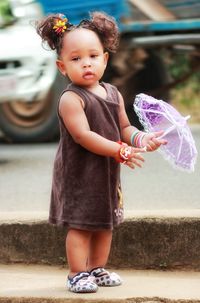 Portrait of cute girl holding toy umbrella while standing on sidewalk