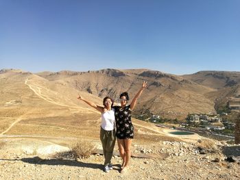 Full length portrait of young couple standing on desert against clear sky