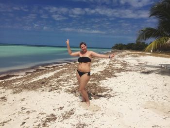 Full length of woman wearing bikini standing at beach against sky