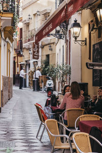 People sitting on sidewalk cafe amidst buildings in city