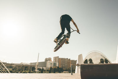 Man riding bicycle on metallic pipe against sky