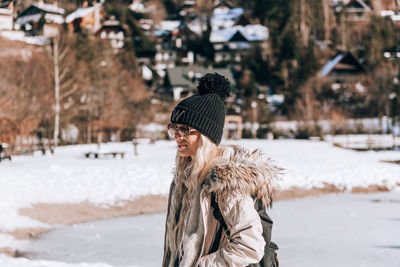 Stylish woman with blond hair, wearing winter clothes, standing on shore of lake jasna in slovenia