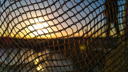 Close-up of chainlink fence against sky during sunset