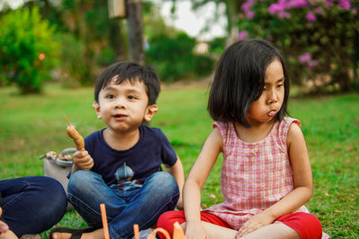 Naughty kids on picnic blanket together in park, playing with food