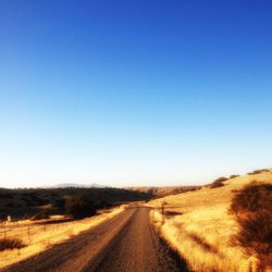 Road passing through field against clear sky