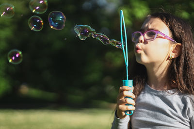 Portrait of a beautiful caucasian girl blows soap bubbles standing in the park