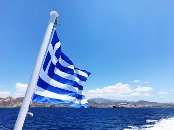 Flag waving in sea against blue sky