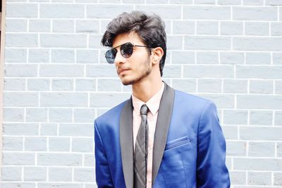 Portrait of young man wearing sunglasses standing against brick wall