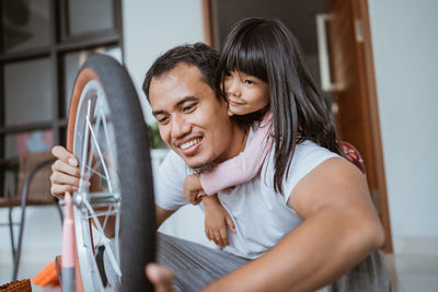 Smiling father repairing bicycle with daughter at home