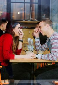 Happy young couple talking while sitting in cafe seen through window