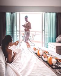 Shirtless man looking at woman on bed at hotel