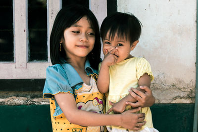 Girl embracing sister against wall