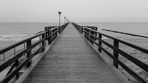 Diminishing perspective of pier over sea against sky