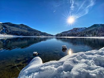 Scenic view of lake by snowcapped mountain against blue sky during winter