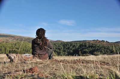 Rear view of man sitting on land against sky