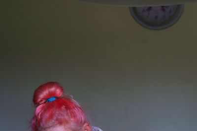 Cropped image of woman with dyed red hair against wall