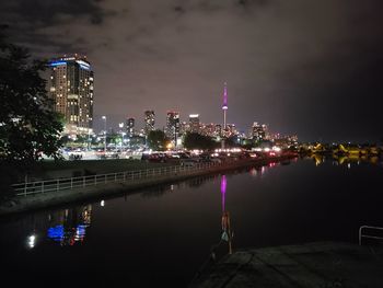 Illuminated buildings by river against sky at night