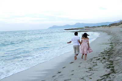 Rear view of friends on beach against sky