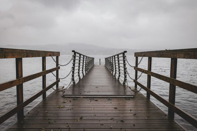 Wooden footbridge on pier against sky