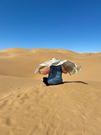 Woman with scarfs on sand dune in desert against clear blue sky