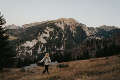 Woman standing by tree on mountain against sky