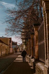 Rear view of person walking on footpath amidst buildings in city