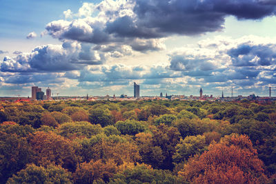 Trees and factory against sky during autumn