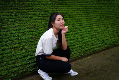 Full length portrait of young woman crouching by wall