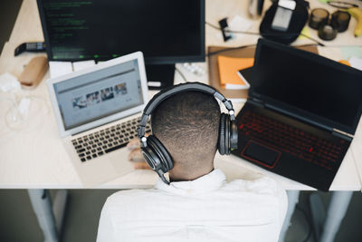 Rear view of male it professional using laptop on desk while sitting in creative office