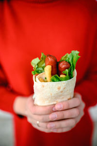 The hands of a girl in red clothes are holding fast street food. shawarma is food in pita
