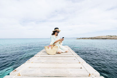 Young woman sitting on pier over sea against sky