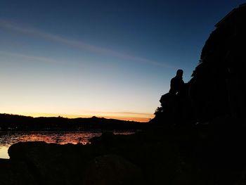 Silhouette of people sitting on rock against sky