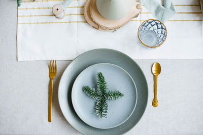 Spruce branch on a plate as part of the table setting with a gold fork and spoon, linen tablecloth