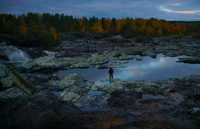 Man standing on rock by trees against sky during autumn