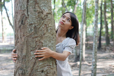 Young woman looking up while standing on tree trunk