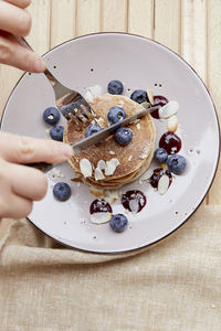 Woman holds cutlery while having breakfast - fresh pancakes with fresh blueberries and agave syrup 