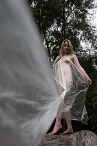 Young naked woman standing on tree trunk in forest