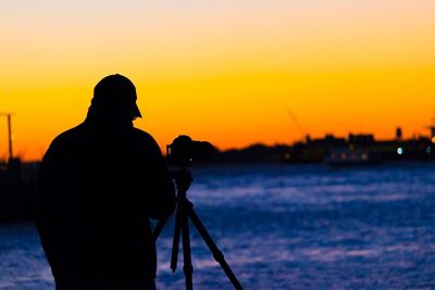 Silhouette man photographing sea against sky during sunset