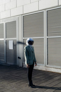 Young businesswoman wearing space helmet by wall