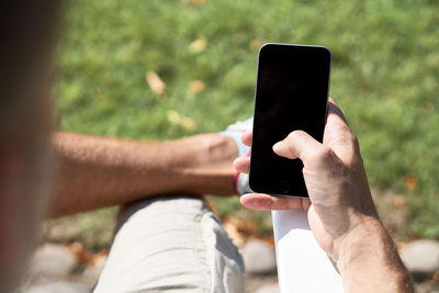 Cropped image of man using blank phone while sitting outdoors