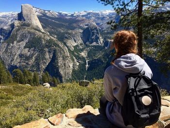 Rear view of woman sitting on rock against sky