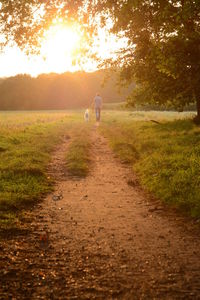 Man walking with dog on dirt road during sunset