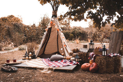 Stylish wigwam with lights, pumpkins and stack of hay outdoors. autumn season.