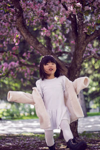 Korean girl in a white light fur coat and a headband stands in a garden with cherry blossoms