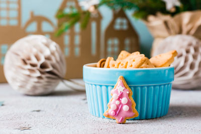 Christmas cookies spruce with pink icing are placed near a bowl of cookies on a decorated table