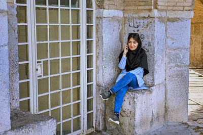 Portrait of young woman sitting against building