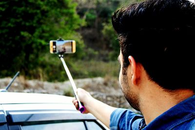 Man holding monopod while taking selfie from mobile phone by car