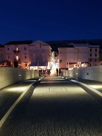 Illuminated street by buildings against clear sky at night