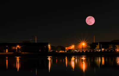 Reflection of illuminated lights in lake against sky at night