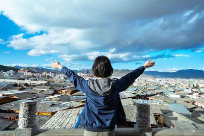 Rear view of woman looking at cityscape against sky